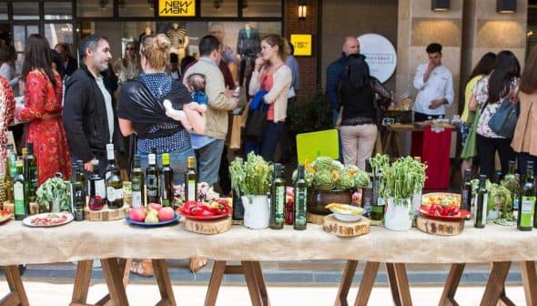 A table featuring various bottles of olive oil and fresh produce at an event. - Olive Oil Times
