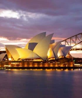 Sydney Opera House illuminated at sunset with the Harbour Bridge in the background. - Olive Oil Times