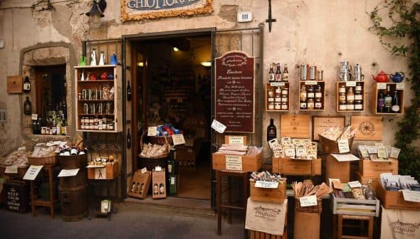 Entrance of a traditional Italian grocery store with various products displayed outside. - Olive Oil Times