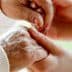 An elderly person's hand being held by a caregiver's hand in a supportive gesture. - Olive Oil Times