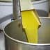 Stream of yellow olive oil being poured from a metal spout into a metal container. - Olive Oil Times