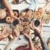 Group of people toasting with glasses over a table filled with various foods and drinks. - Olive Oil Times