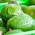Fresh green avocados displayed in green plastic baskets at a market. - Olive Oil Times