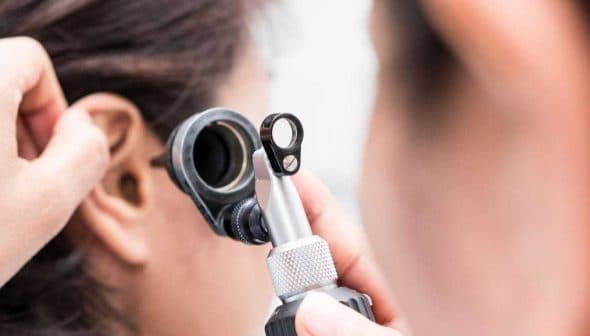 Healthcare professional examining a patient's ear with an otoscope in a clinical setting. - Olive Oil Times