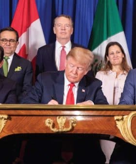 Political leaders signing the USMCA agreement at a table with flags of the US, Canada, and Mexico in the background. - Olive Oil Times