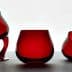 Three pieces of red glassware including a curved glass, a round glass, and a tilted glass. - Olive Oil Times