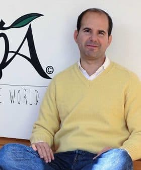 Man wearing a yellow sweater sitting on the floor in front of the LOA logo. - Olive Oil Times