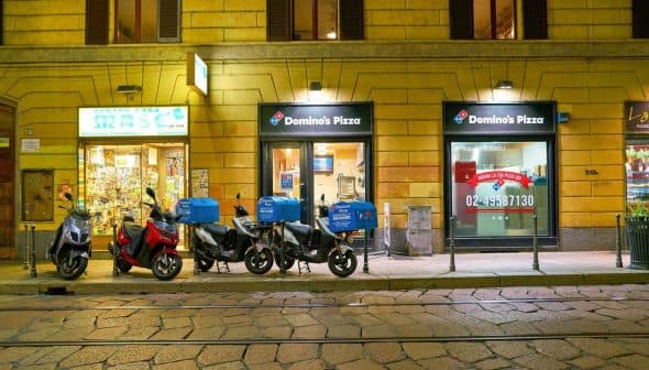 Row of delivery motorcycles parked outside a Domino's Pizza location at night. - Olive Oil Times