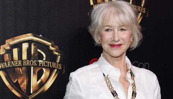 Woman with short gray hair wearing a white shirt and necklace at a Warner Bros. Pictures event backdrop. - Olive Oil Times