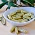 A white dish containing green herbal capsules, surrounded by leaves on a wooden surface. - Olive Oil Times