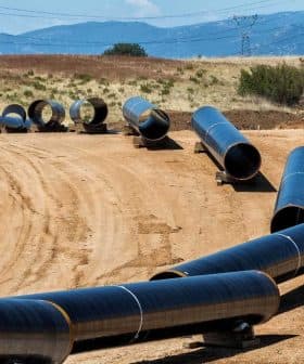 Several black pipeline sections laid out on a construction site with a dirt surface. - Olive Oil Times