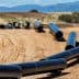 Several black pipeline sections laid out on a construction site with a dirt surface. - Olive Oil Times
