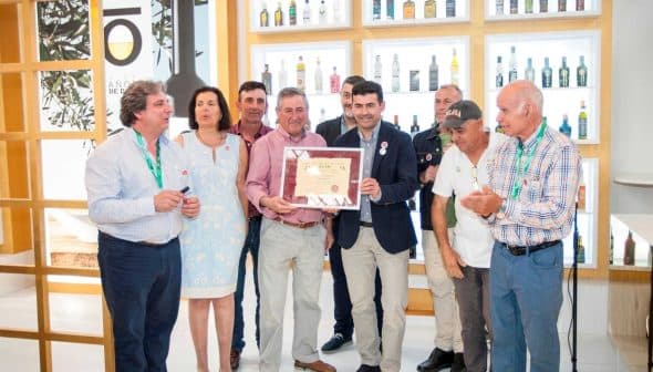 A group of individuals standing together, holding an award certificate in a well-lit indoor setting. - Olive Oil Times