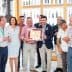 A group of individuals standing together, holding an award certificate in a well-lit indoor setting. - Olive Oil Times