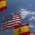 Spanish flags and an American flag waving in the wind against a blue sky with clouds. - Olive Oil Times