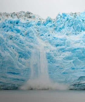 A large glacier with a waterfall cascading down its icy surface into the water below. - Olive Oil Times