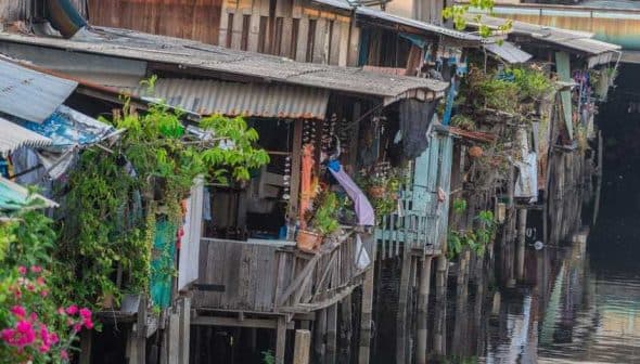 Wooden houses on stilts along a waterway, featuring plants and clothes hanging outside. - Olive Oil Times