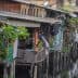 Wooden houses on stilts along a waterway, featuring plants and clothes hanging outside. - Olive Oil Times