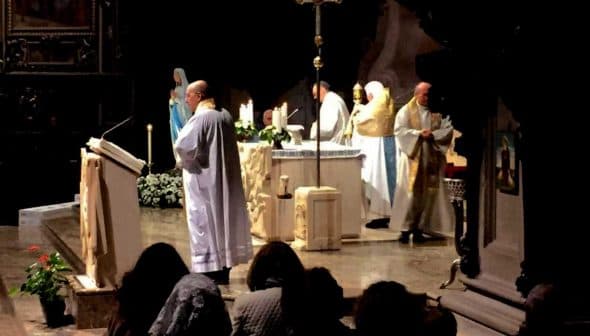 Clergy members conducting a religious ceremony at an altar with candles and decorations. - Olive Oil Times