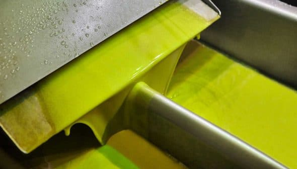 Green olive oil flowing from a metal spout during the extraction process. - Olive Oil Times