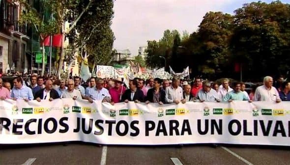 Group of people marching in a protest holding a large banner that reads 'Precios Justos Para Un Olivar'. - Olive Oil Times