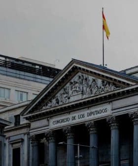 The Congreso de los Diputados building in Spain with a statue in front and a flag on top. - Olive Oil Times