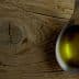 Metal spoon filled with olive oil resting on a textured wooden surface. - Olive Oil Times