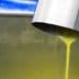 Stream of yellow olive oil pouring from a metal spout into a container. - Olive Oil Times