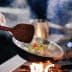 Chef using a wooden spatula to stir colorful vegetables in a frying pan over a flame. - Olive Oil Times