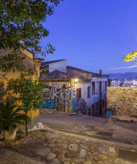 Narrow street featuring graffiti on a wall and buildings under evening light. - Olive Oil Times