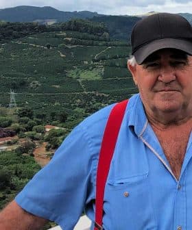 Man wearing a blue shirt and red suspenders standing outdoors with green hills in the background. - Olive Oil Times