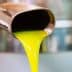 Stream of bright yellow olive oil pouring from a metal spout into a container. - Olive Oil Times
