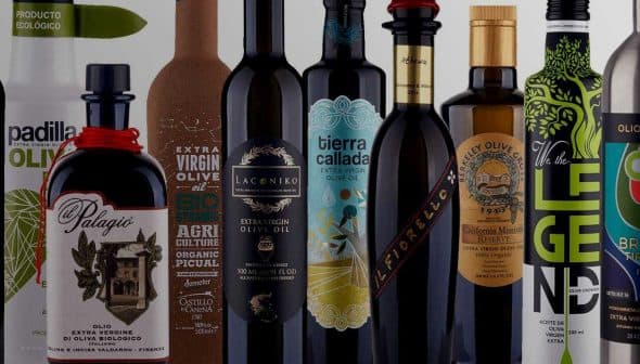 A collection of olive oil bottles with distinct labels and designs arranged in a row. - Olive Oil Times