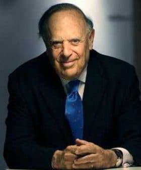 A man in a suit with a blue tie sitting at a table, smiling at the camera. - Olive Oil Times