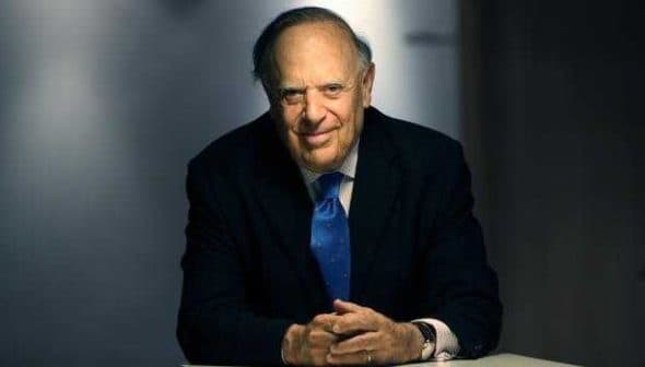 A man in a suit with a blue tie sitting at a table, smiling at the camera. - Olive Oil Times