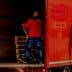A man in a red jacket loading wooden pallets into the back of a red delivery truck. - Olive Oil Times