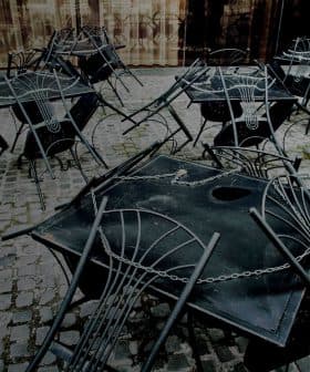 Several black metal tables and chairs stacked on a cobblestone surface. - Olive Oil Times