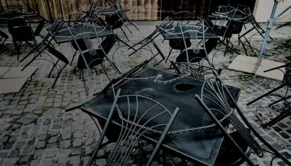Several black metal tables and chairs stacked on a cobblestone surface. - Olive Oil Times