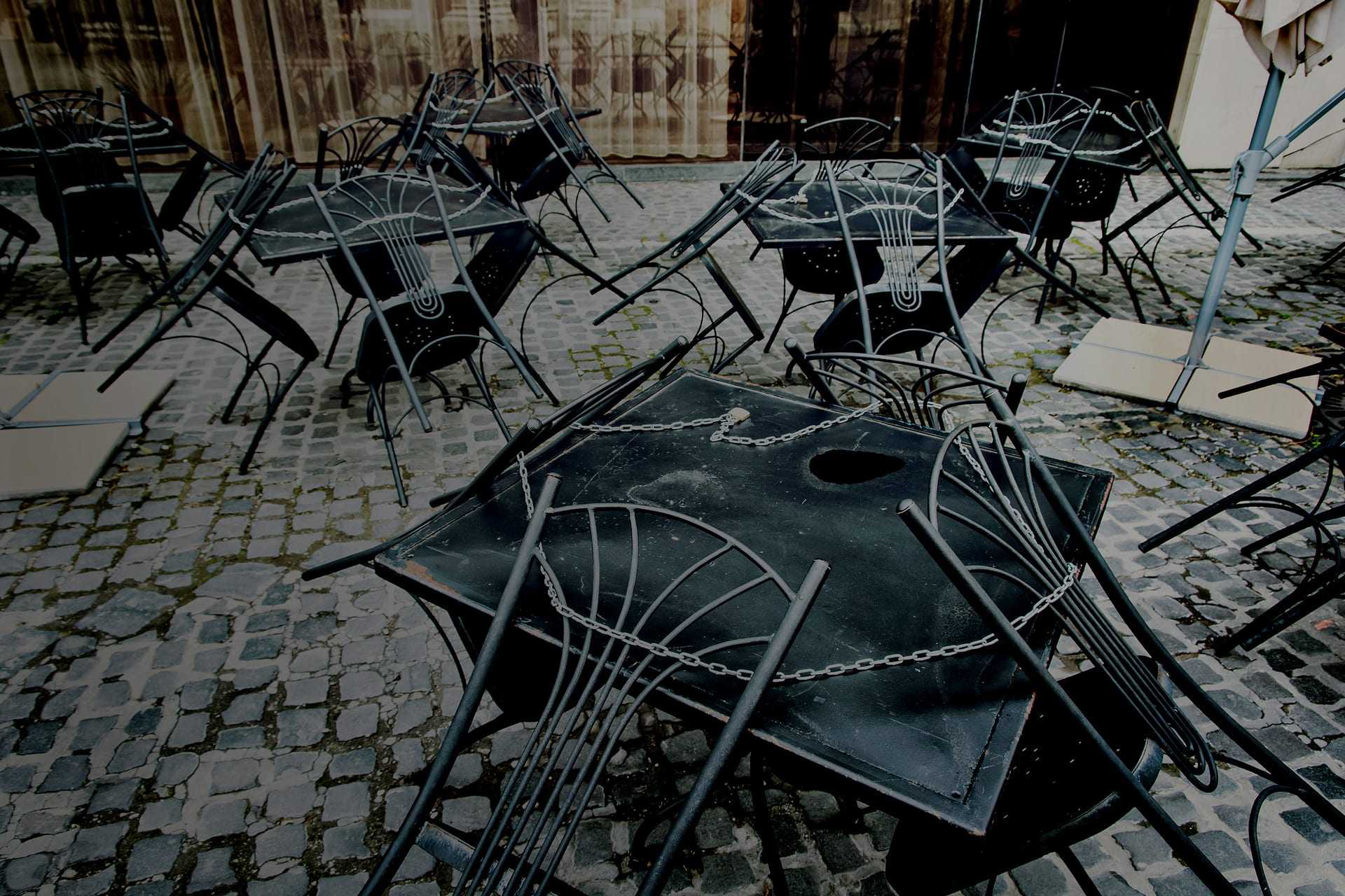 Several black metal tables and chairs stacked on a cobblestone surface. - Olive Oil Times
