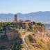 Aerial view of Civita di Bagnoregio, an ancient hilltop village in Italy, surrounded by mountains and valleys. - Olive Oil Times