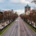 Wide view of an empty city street lined with bare trees and streetlights on either side. - Olive Oil Times