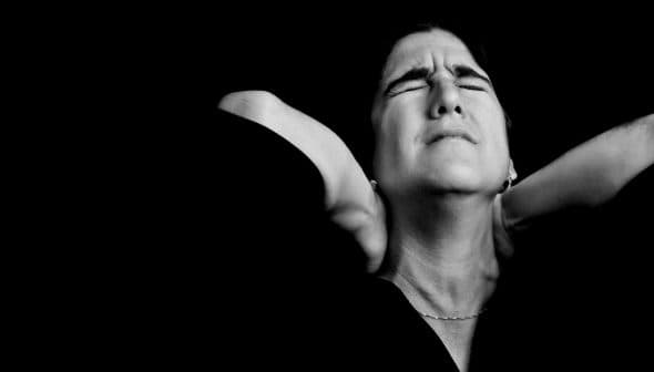 Black and white portrait of a woman with closed eyes and hands on her neck, expressing a moment of contemplation. - Olive Oil Times