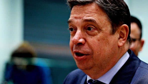 A man in a dark suit speaking during a formal event or meeting. - Olive Oil Times