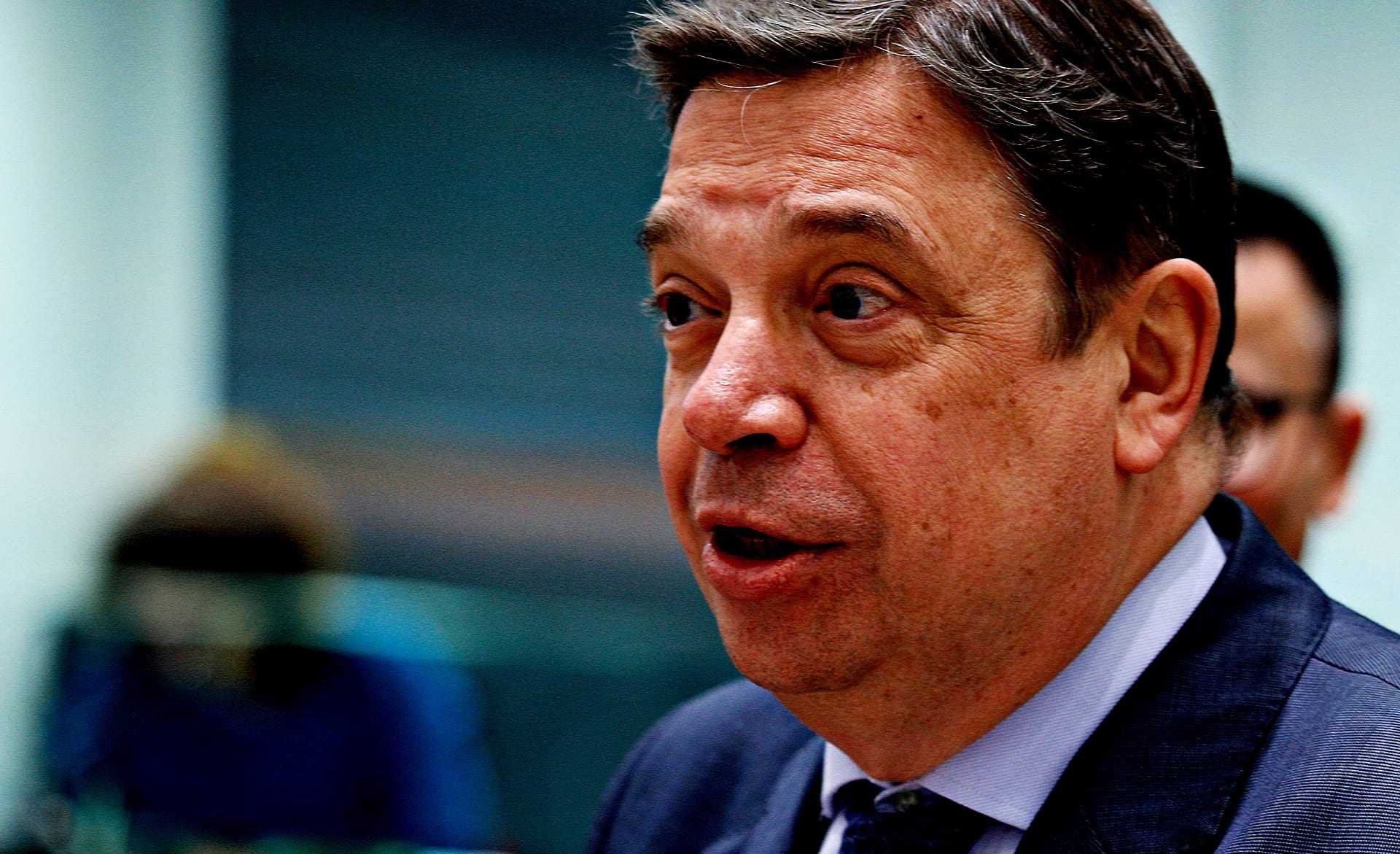 A man in a dark suit speaking during a formal event or meeting. - Olive Oil Times