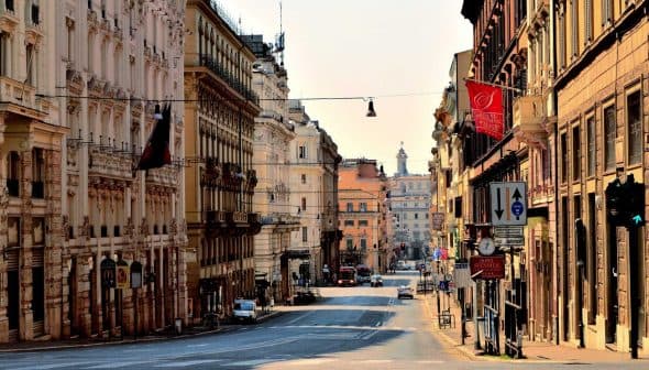 View of a wide, empty street in Rome with buildings lining both sides and traffic signals visible. - Olive Oil Times