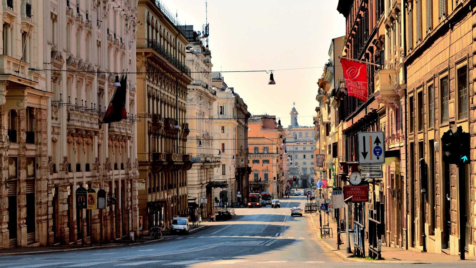 View of a wide, empty street in Rome with buildings lining both sides and traffic signals visible. - Olive Oil Times
