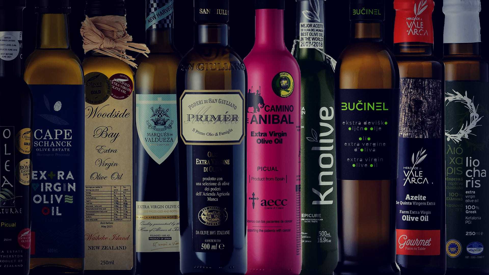 A collection of olive oil bottles with different labels and designs arranged in a row. - Olive Oil Times