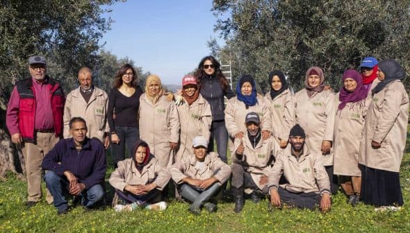 A group of olive harvest workers posing together outdoors in olive trees. - Olive Oil Times