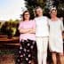 Three women standing together in an olive grove, wearing casual clothing and smiling at the camera. - Olive Oil Times