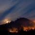 A mountain landscape with visible flames and smoke under a night sky with clouds and a full moon. - Olive Oil Times